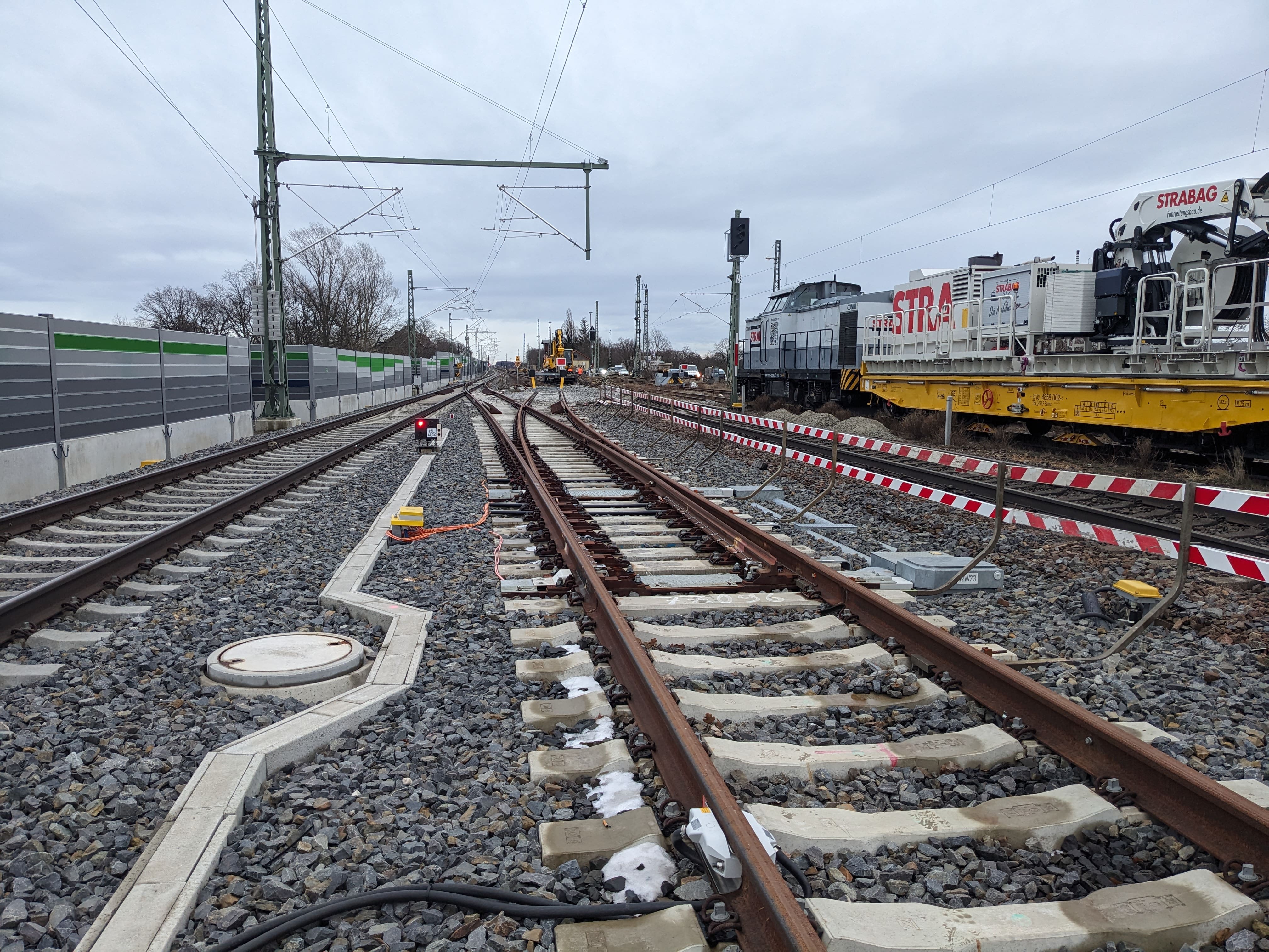 Links Schallschutzwände, Schotterbett mit Gleisen, rechts Baumaschine