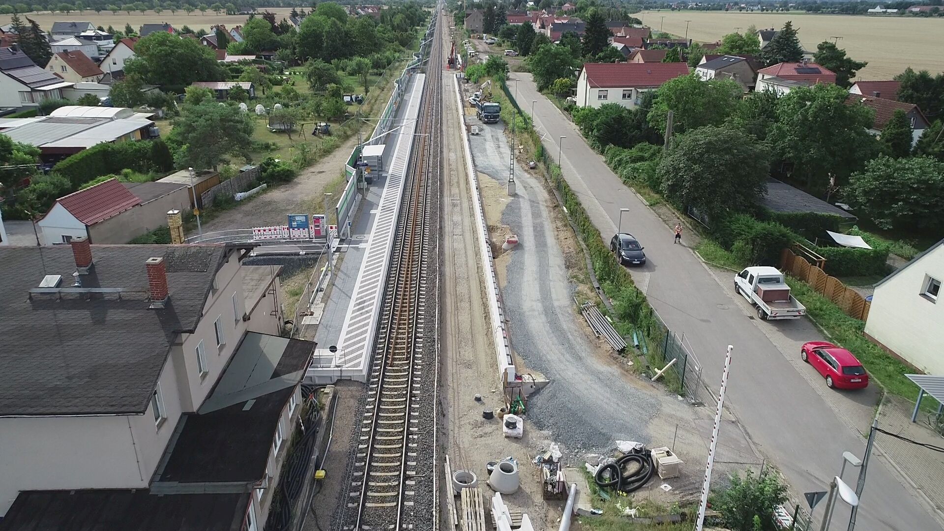 Luftaufnahme mit Blick auf Bahnsteige in Glaubitz, rechts und links der Gleise Häuser, rechts Straße mit Autos