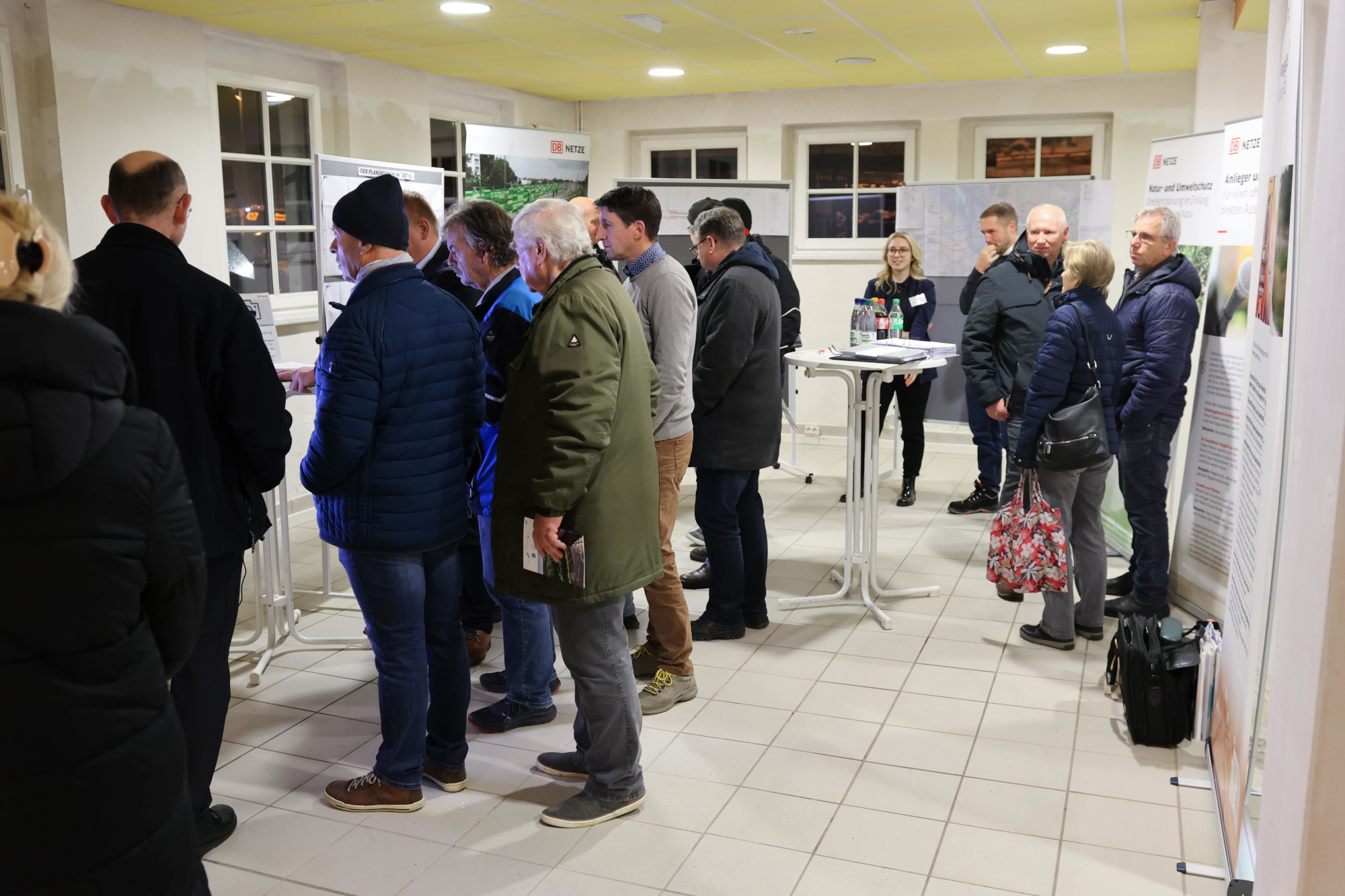 Eine Gruppe von Menschen steht in einem Raum. Es sind Roll-Ups und Pinnwände zu sehen.