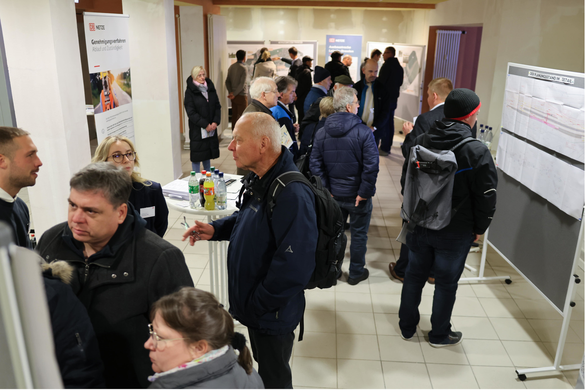 Eine Gruppe von Menschen steht in einem Raum. Es sind Pinnwände und Roll-Ups zu sehen.