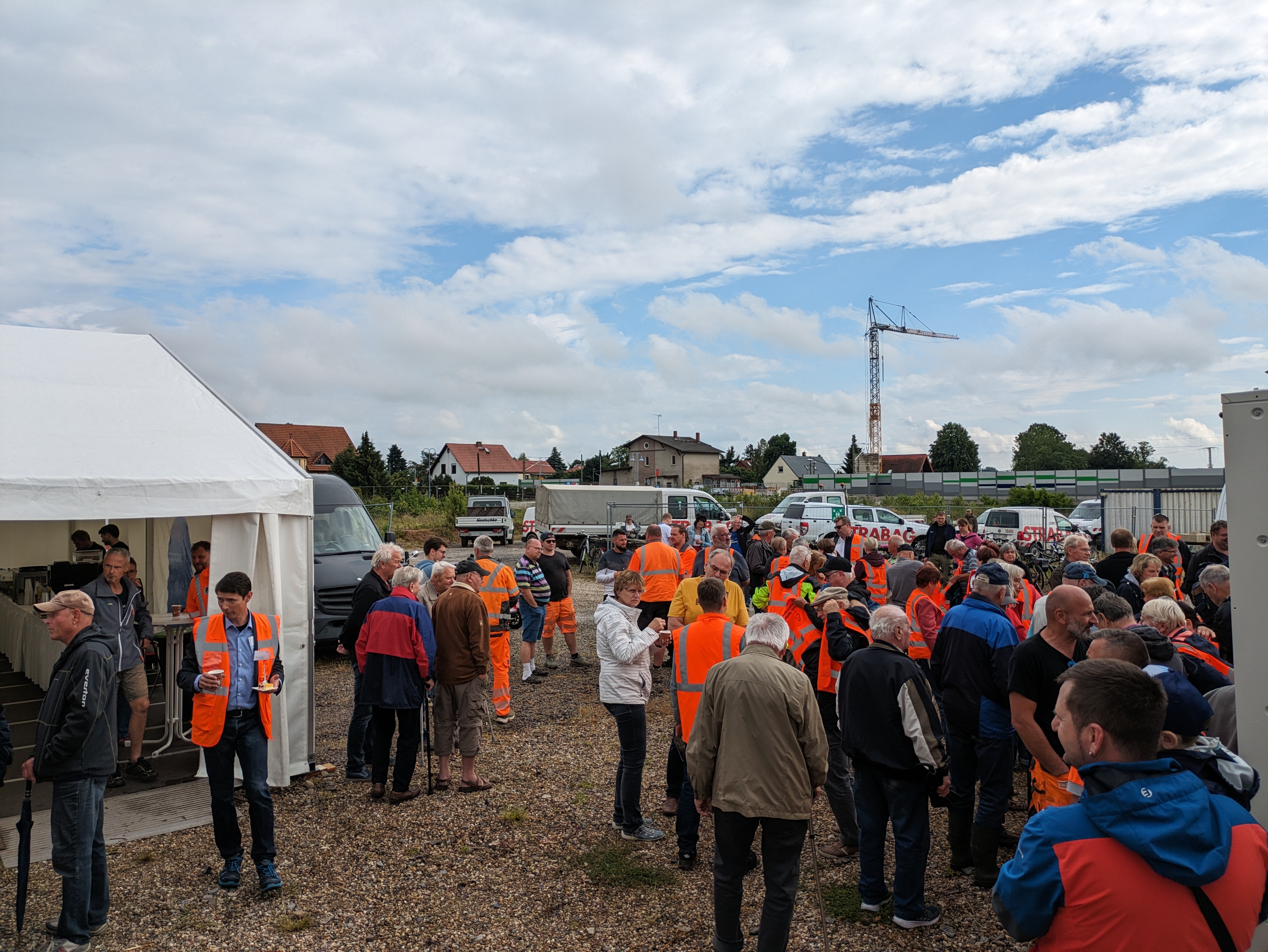 Viele Menschen mit Getränken und Speisen stehen auf der Baustelleneinrichtungsfläche in Glaubitz neben dem Zelt.